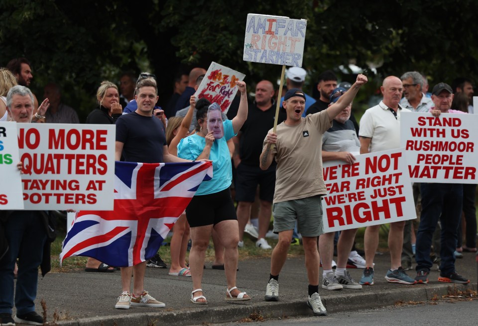 Demonstrators holding signs during a protest outside the Potters International Hotel which houses migrants in Aldershot