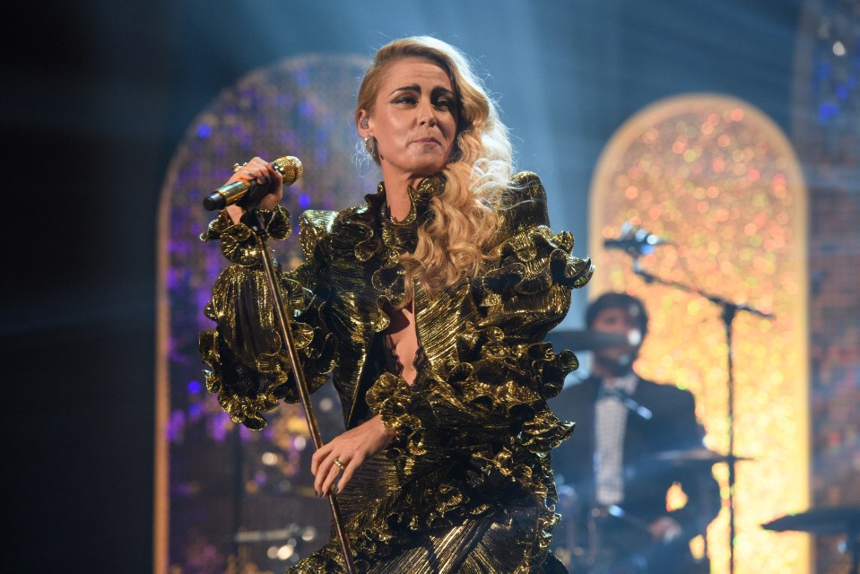 a woman in a gold dress singing into a microphone