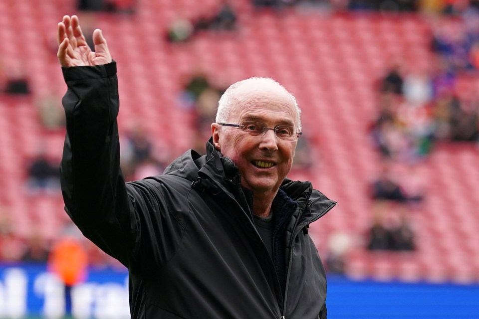 a man wearing glasses and a black jacket waves his hand