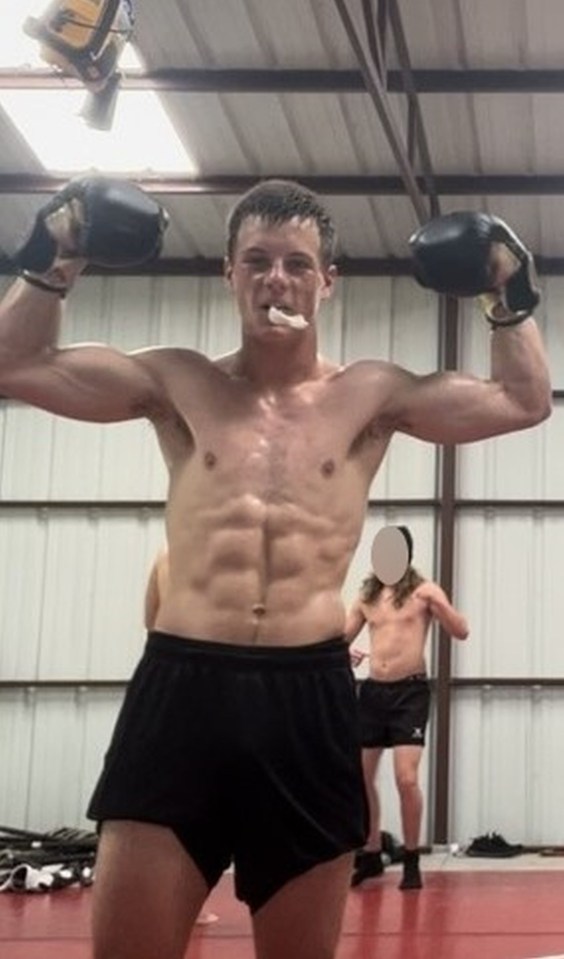 a shirtless man wearing boxing gloves stands in a gym