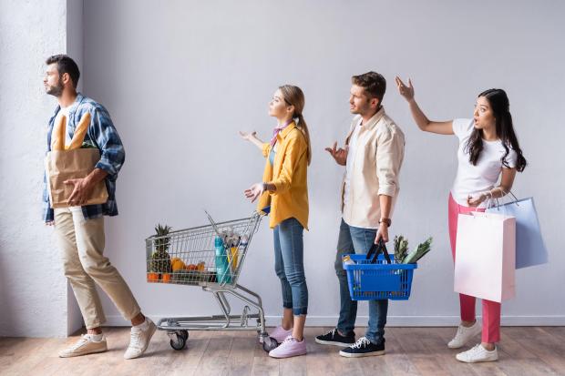 a group of people are standing in a line holding shopping bags and shopping carts