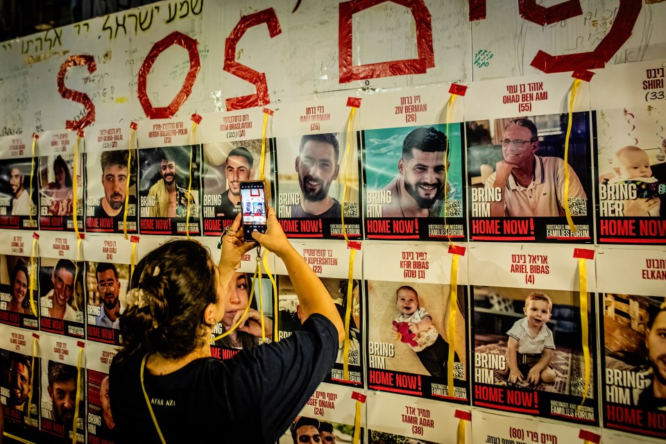 a woman taking a picture of a wall of posters that say bring him home now