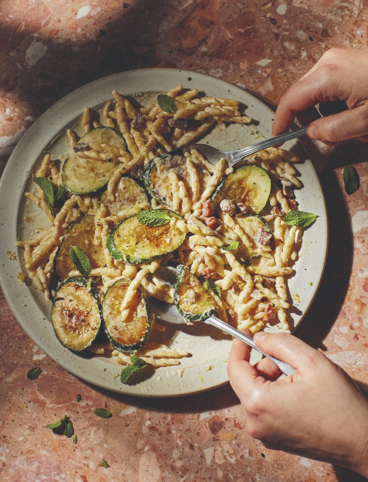 a person is eating pasta with zucchini on a plate