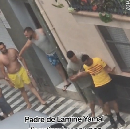 a group of men standing on a sidewalk with the words padre de lamine yamal discussing with unos vecinos del barrio