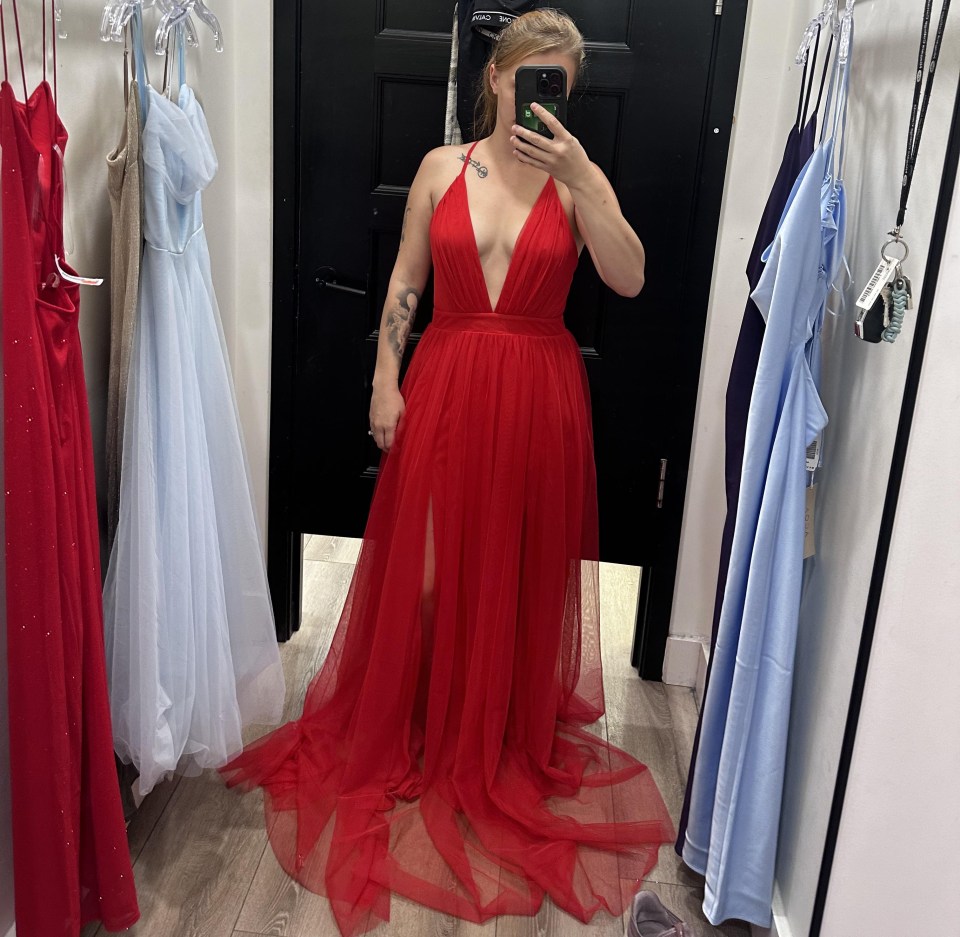 a woman in a red dress is taking a selfie in a dressing room