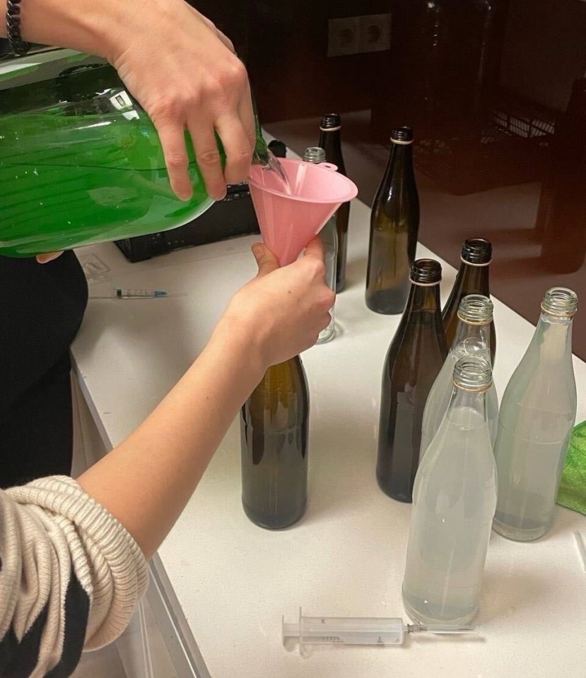 a person pouring liquid into a bottle with a pink funnel