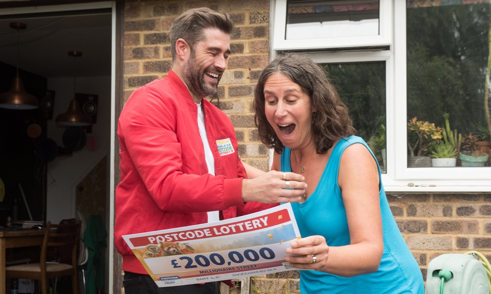 a man in a red jacket is giving a woman a postcode lottery ticket