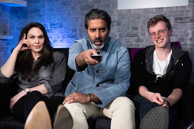 a man is holding a remote control while sitting on a couch with two other people