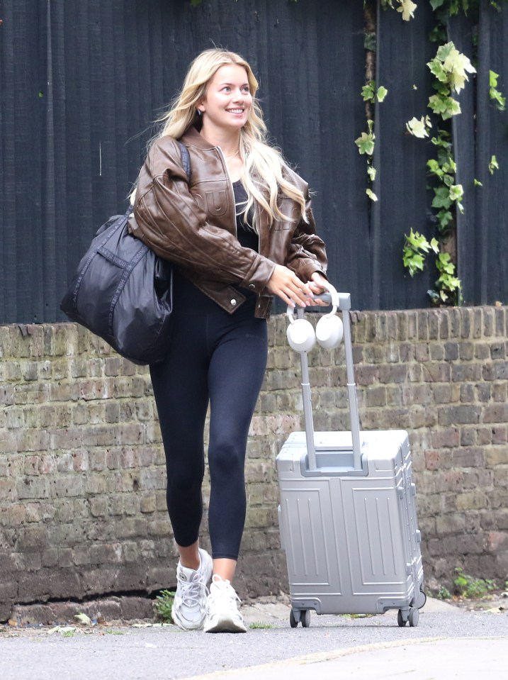 a woman carrying a suitcase and headphones is smiling