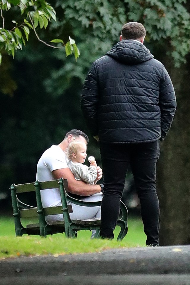 a man holding a baby while another man looks on