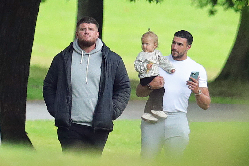 a man holding a baby while another man looks at his phone