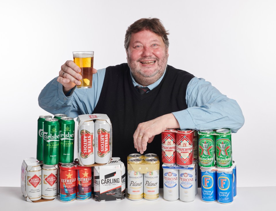 a man holds a glass of beer in front of several cans of beer including carlsberg stella artois and estrella damm