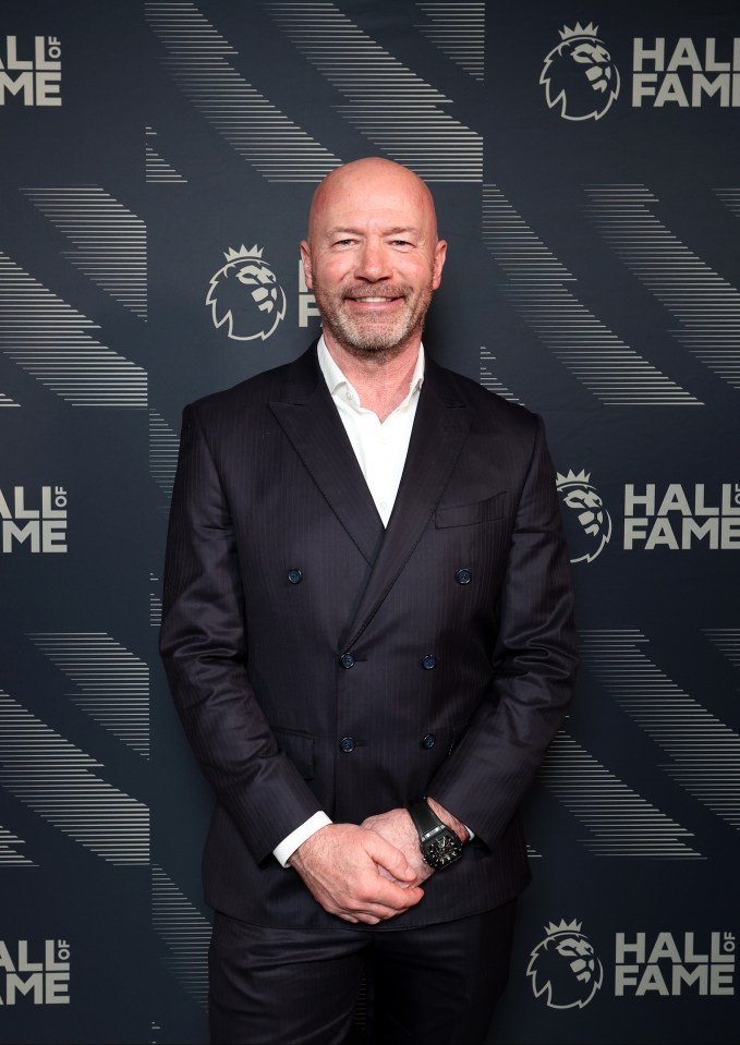 a man in a suit stands in front of a wall that says hall of fame