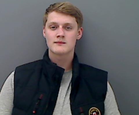 a young man wearing a black vest and a white shirt is standing in front of a wall .