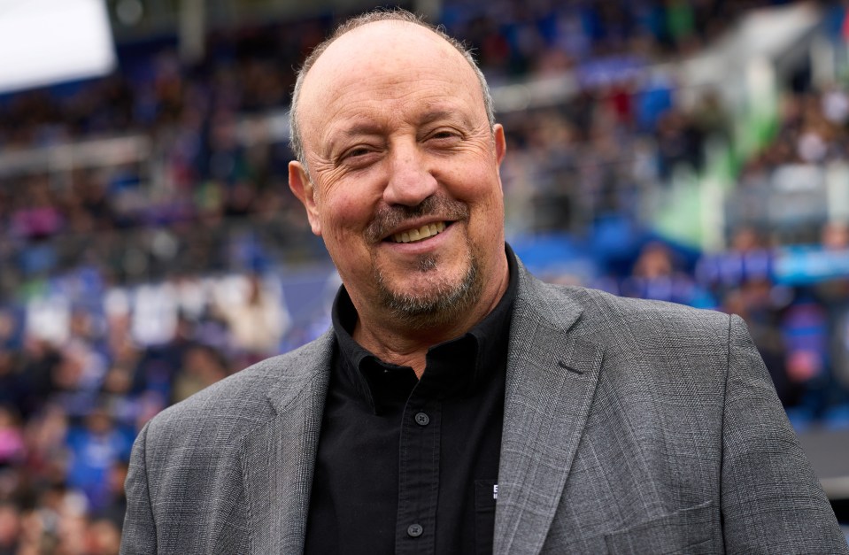 a man in a suit and black shirt smiles in front of a crowd