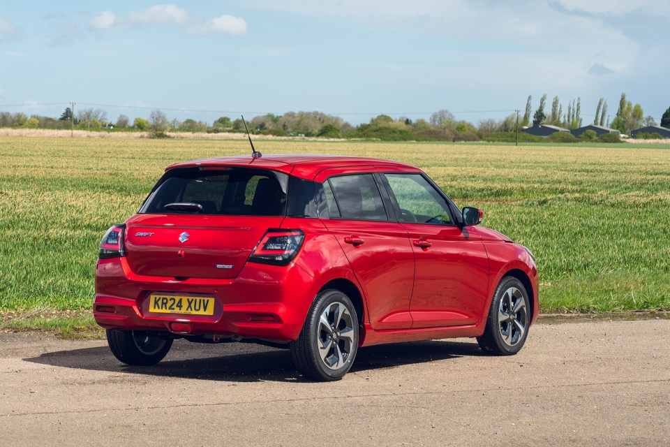 a red suzuki car is parked on the side of the road