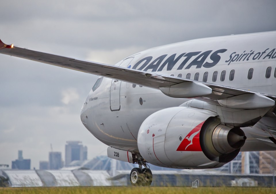 a qantas plane sits on a runway with a city in the background