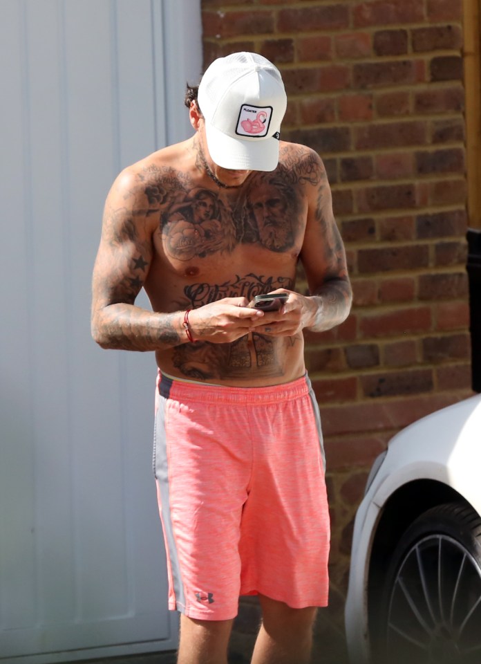 a shirtless man wearing a white hat and pink shorts looks at his phone