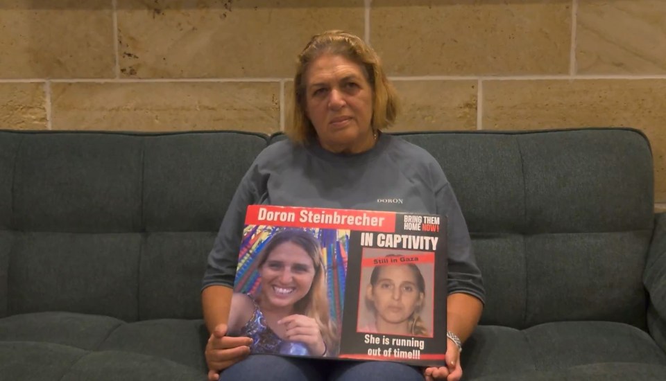 a woman sits on a couch holding a sign that says doron steinbrecher in captivity