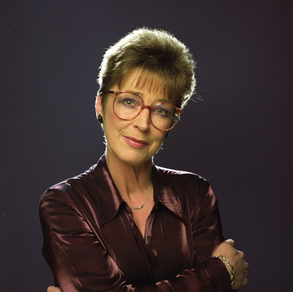 a woman wearing glasses stands with her arms crossed