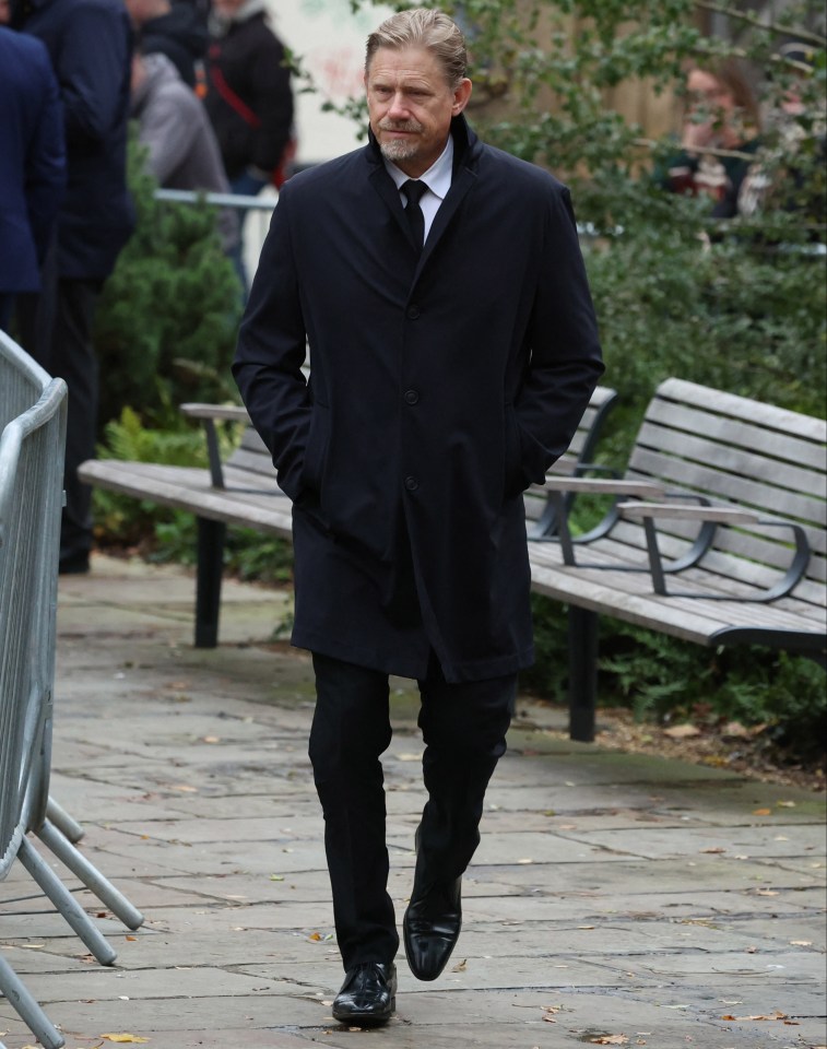 a man in a black coat and tie walks down a sidewalk