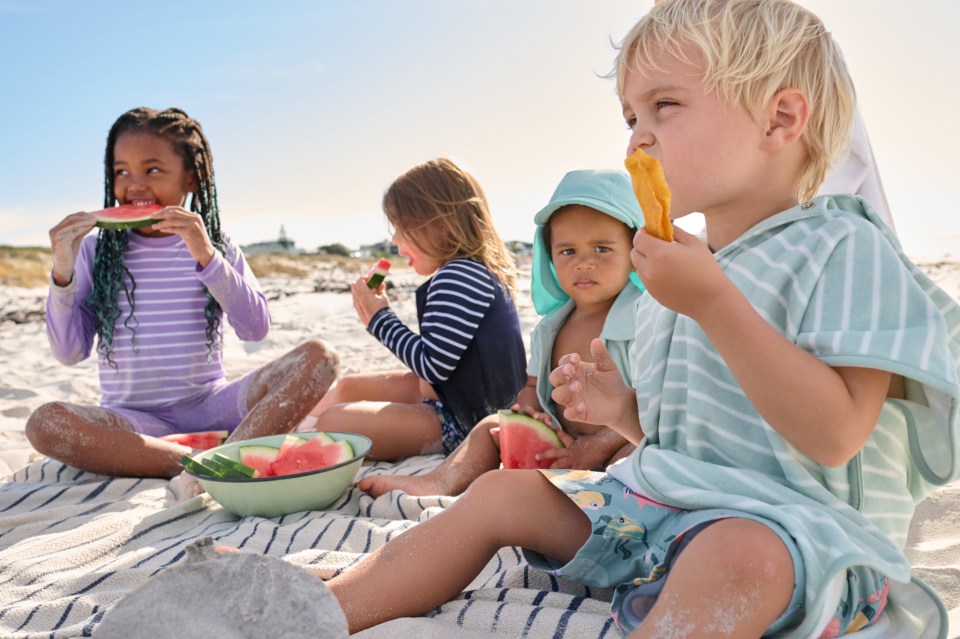 a group of children are eating watermelon on the beach