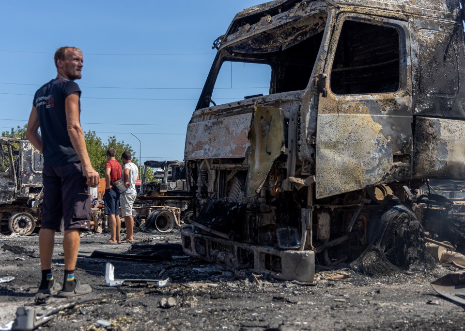 TOPSHOT - People look at burnt-out trucks on a site following an air attack, in the Odesa region, on August 26, 2024, amid the Russian invasion of Ukraine. Russian drones and missiles on August 26, 2024 targeted 15 regions across Ukraine in an overnight barrage aimed mainly at energy infrastructure, Ukrainian Prime Minister Denys Shmygal said. (Photo by Oleksandr GIMANOV / AFP) (Photo by OLEKSANDR GIMANOV/AFP via Getty Images)