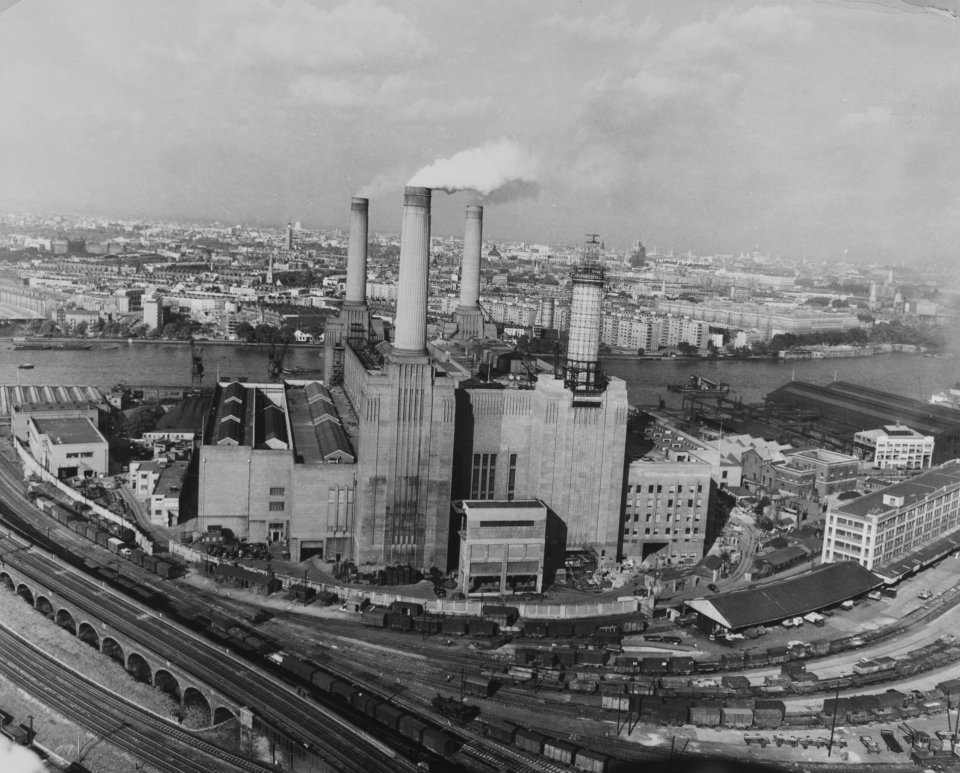 a black and white photo of a factory with smoke coming out of the chimneys