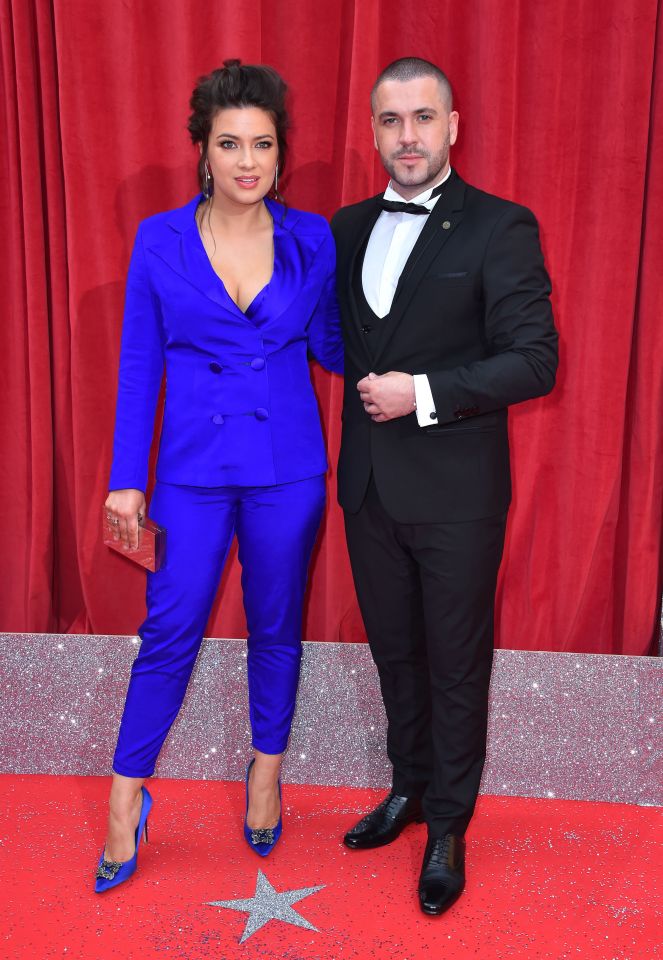 a woman in a blue suit stands next to a man in a tuxedo on a red carpet