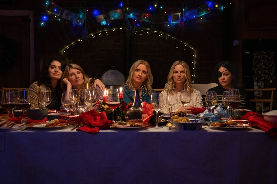 a group of women sit at a long table with plates of food and wine glasses