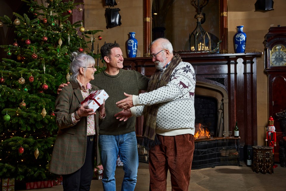 a man giving a gift to an older couple in front of a christmas tree