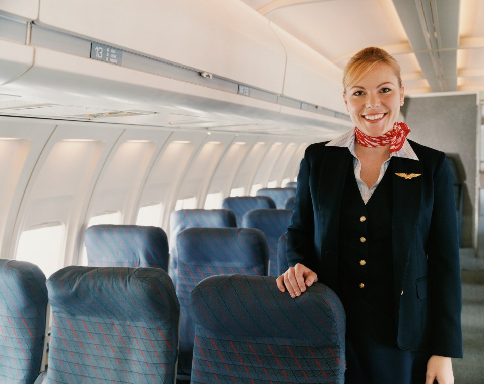 a smiling stewardess stands in an airplane with the number 13 on the ceiling