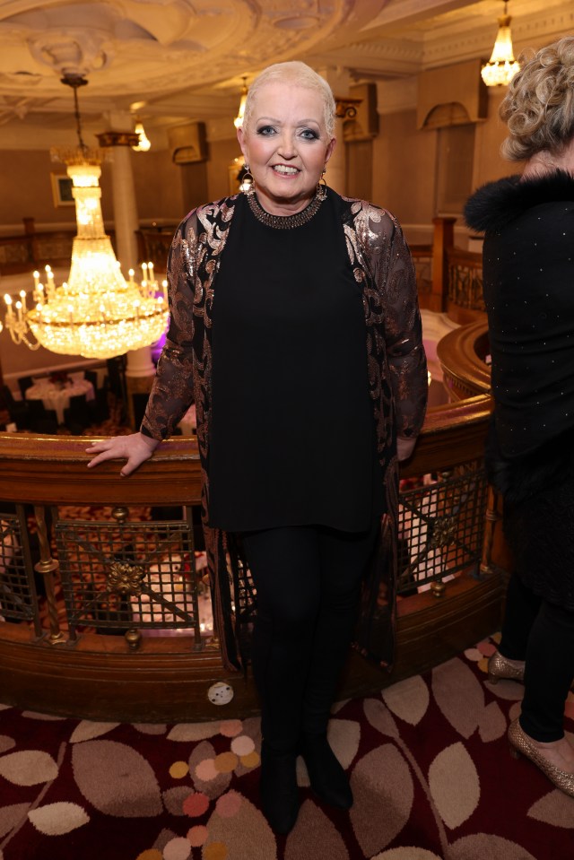 a woman in a black top and brown jacket stands on a balcony