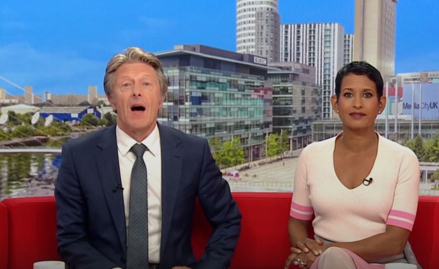 a man and a woman are sitting in front of a bbc building