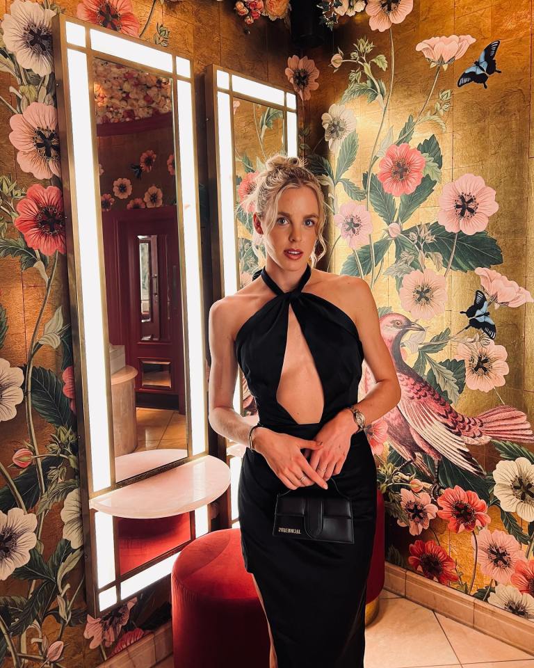 Keely Hodgkinson in a black halter dress, holding a small black purse, standing in front of a floral-patterned wall with mirrors.