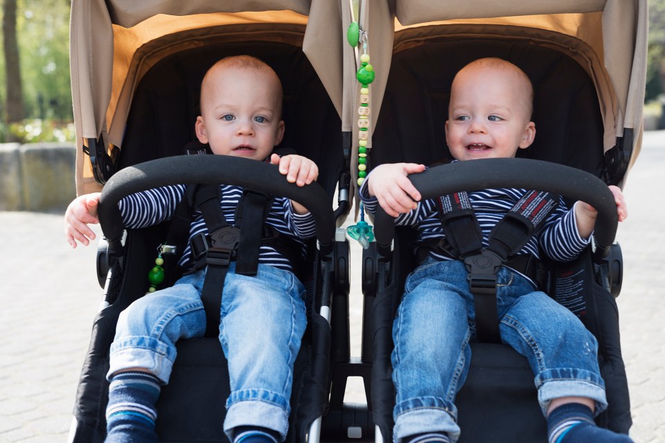 two babies are sitting in a stroller and one has a pacifier hanging from the handle