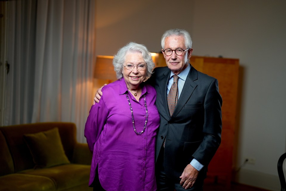 a man in a suit stands next to a woman in a purple shirt