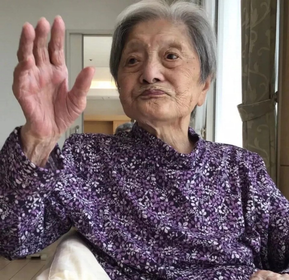 an elderly woman in a purple shirt waves her hand