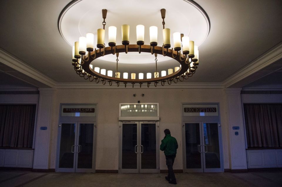 a man in a green jacket stands under a large chandelier in front of a sign that says reception