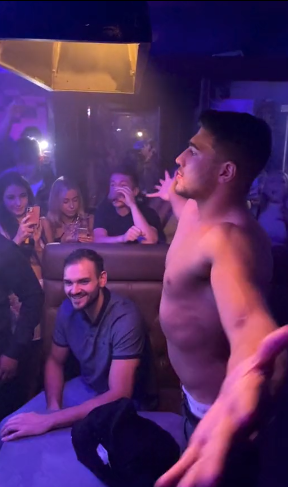 a shirtless man is dancing in front of a crowd of people in a bar .