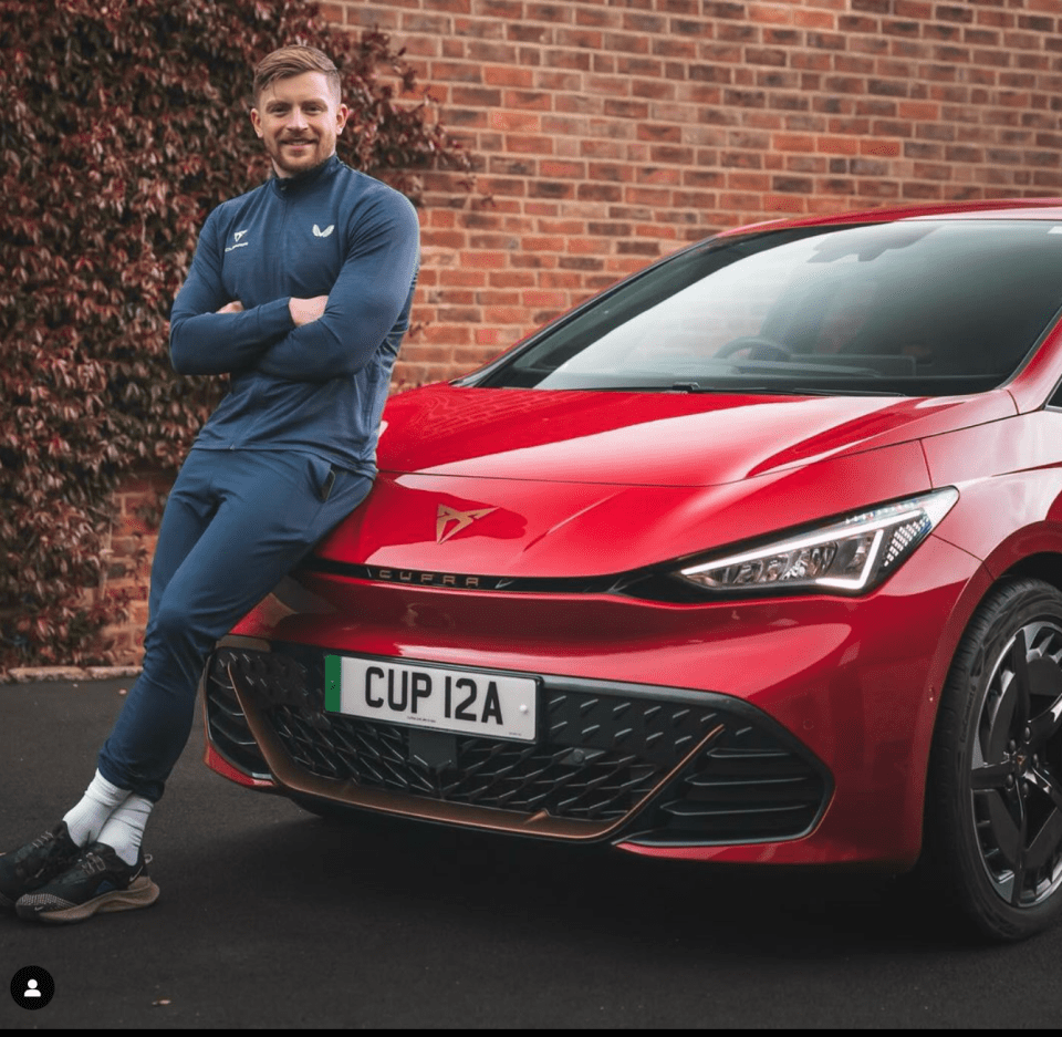 a man leans against a red car with a license plate that says cup 12a