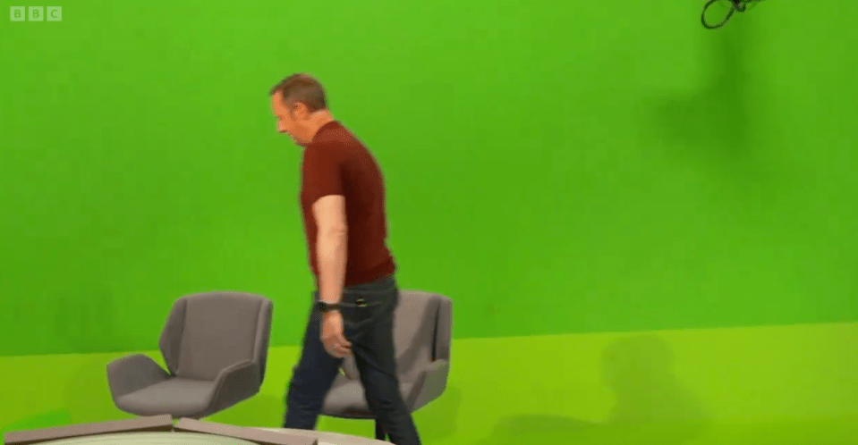 a man in a red shirt stands in front of a green screen that says bbc