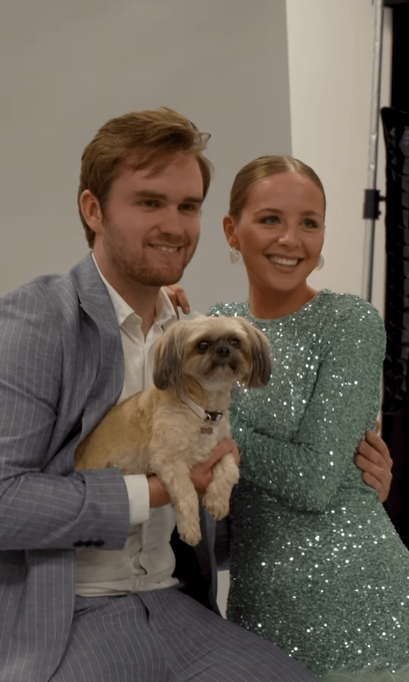 a man in a suit holds a small dog next to a woman in a green dress