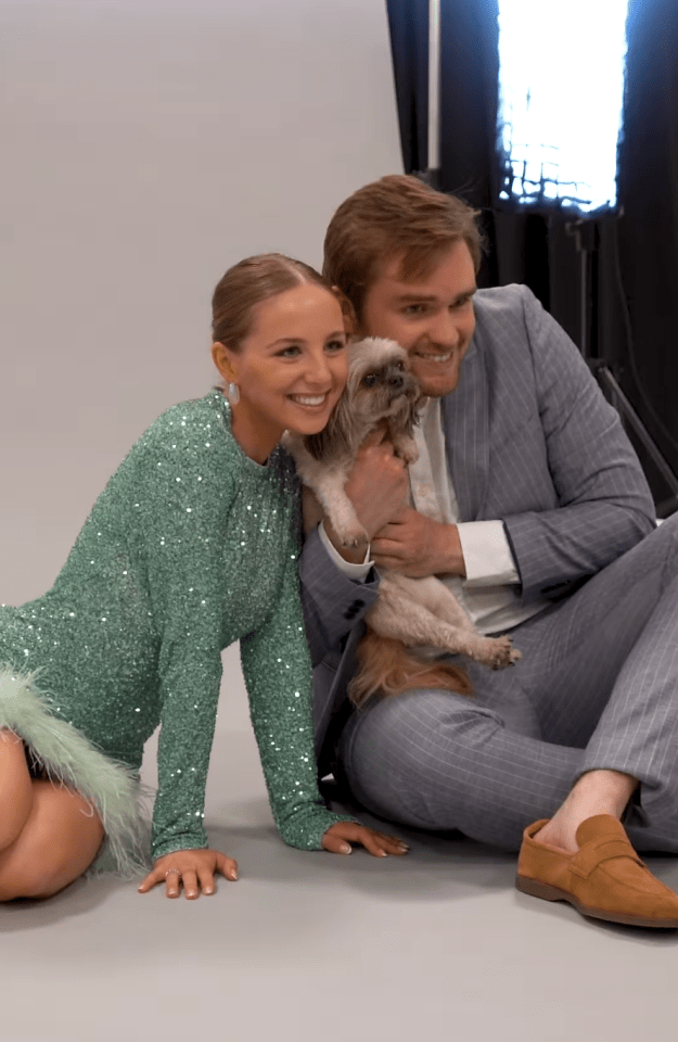 a woman in a green dress sits next to a man in a suit holding a small dog