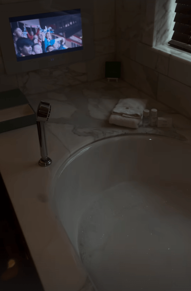 a bathtub with a tv on the wall above it