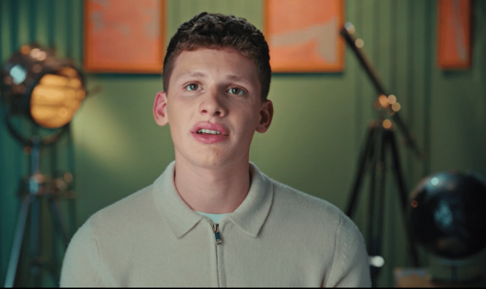 a young man in a white sweater looks at the camera