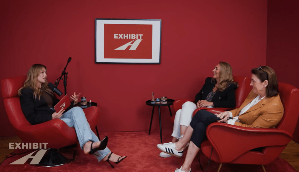 three women sit in red chairs in front of a sign that says exhibit a