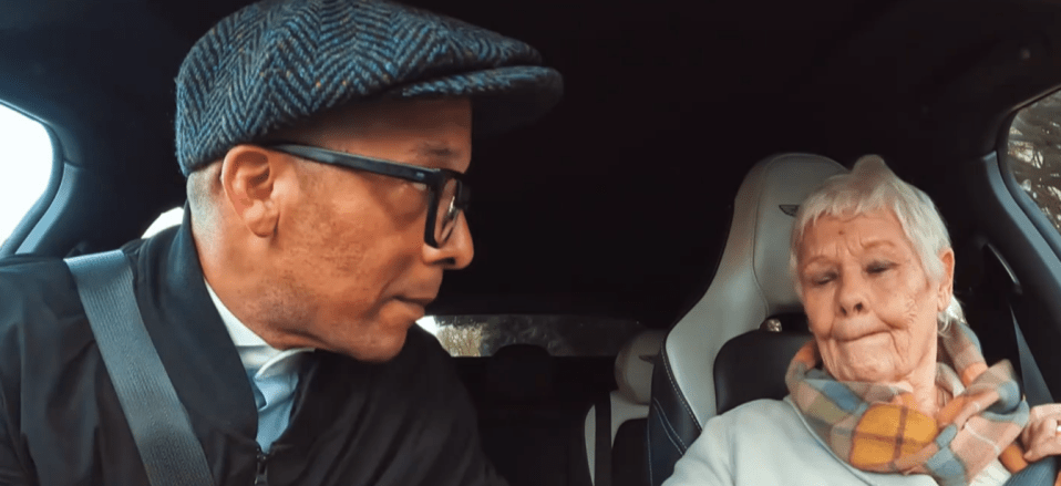 a man wearing glasses is talking to an older woman in a car