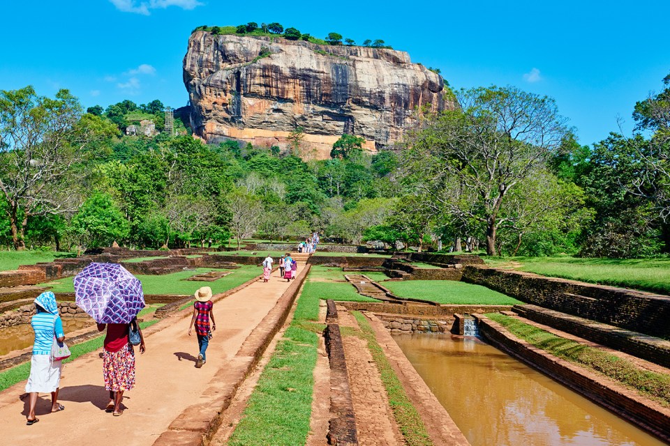 a group of people walking down a path with a large rock in the background