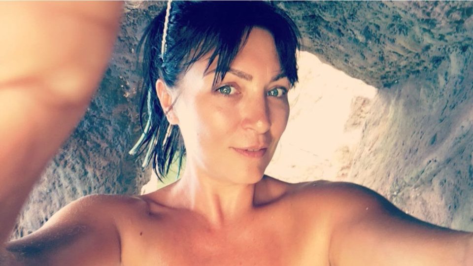 a woman without a shirt is taking a selfie in a cave